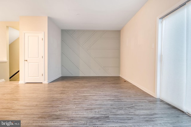 spare room with wood finished floors, baseboards, and a decorative wall