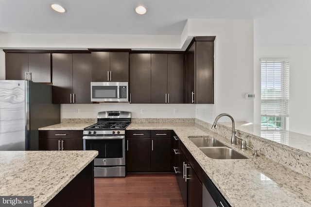 kitchen featuring appliances with stainless steel finishes, a sink, light stone counters, recessed lighting, and dark wood-style flooring