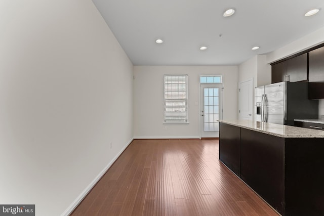 kitchen featuring stainless steel refrigerator with ice dispenser, baseboards, dark wood finished floors, recessed lighting, and light stone counters