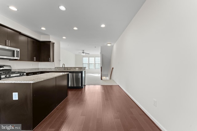 kitchen featuring stainless steel appliances, a sink, recessed lighting, a peninsula, and dark wood-type flooring