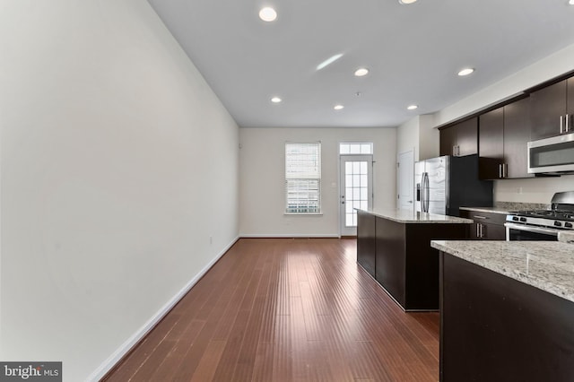 kitchen with appliances with stainless steel finishes, baseboards, a kitchen island, recessed lighting, and dark wood-type flooring