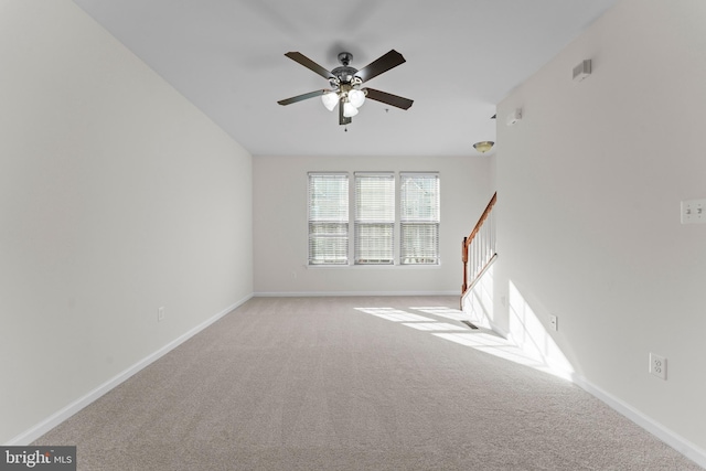 spare room featuring carpet flooring, a ceiling fan, stairway, and baseboards