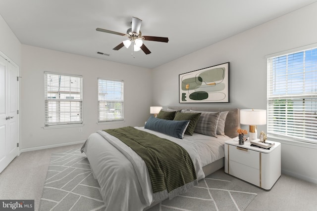 bedroom featuring light carpet, baseboards, multiple windows, and ceiling fan