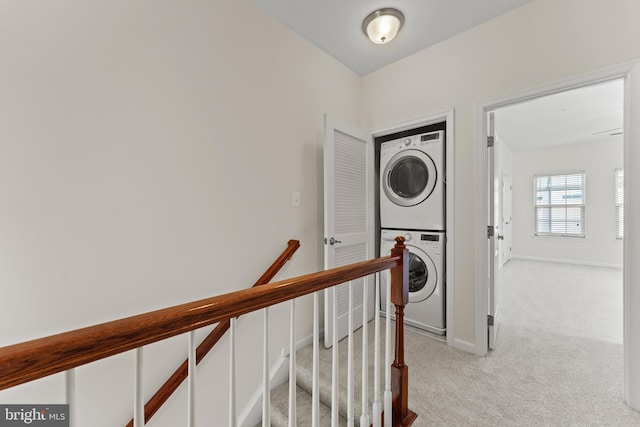 hallway with estacked washer and dryer, light carpet, an upstairs landing, and baseboards