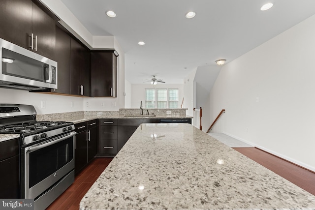 kitchen featuring stainless steel appliances, a sink, dark wood-style floors, light stone countertops, and recessed lighting