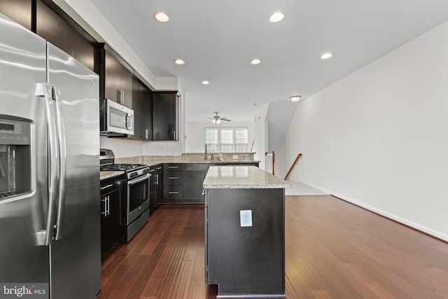 kitchen featuring stainless steel appliances, a sink, a peninsula, recessed lighting, and light stone counters