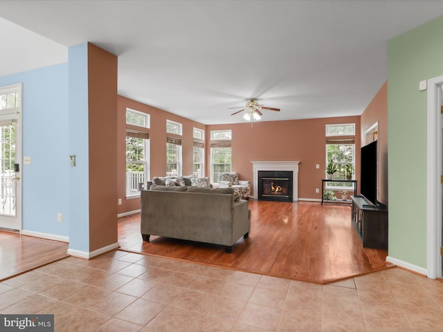 9499 Ballagan Ct, Bristow, VA 20136 - living room featuring light tile patterned floors, ceiling fan, a glass covered fireplace, and plenty of natural light