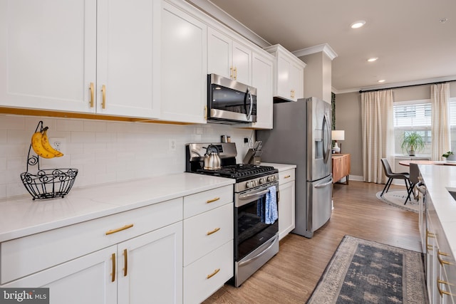 kitchen with appliances with stainless steel finishes, ornamental molding, white cabinets, light wood-type flooring, and decorative backsplash