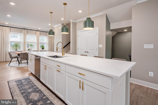 kitchen with a sink, light wood-style floors, white cabinetry, an island with sink, and pendant lighting