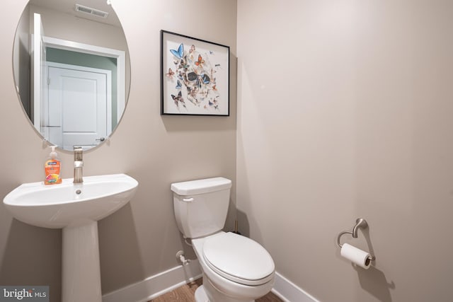 half bath with baseboards, toilet, and wood finished floors