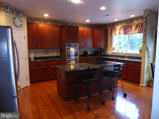 kitchen with appliances with stainless steel finishes, a sink, a kitchen breakfast bar, light wood-style flooring, and a center island
