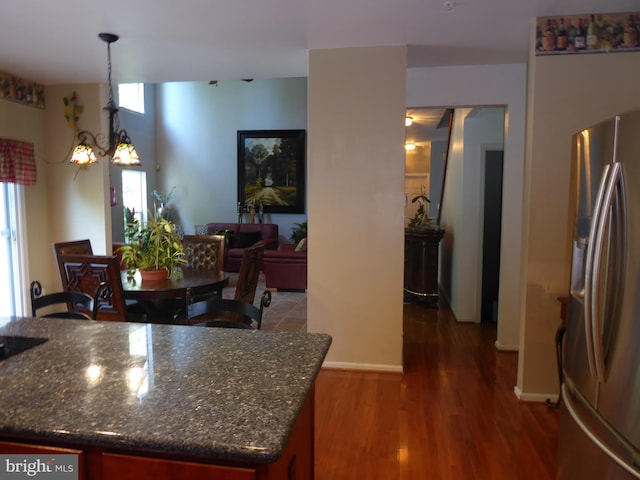 kitchen featuring stainless steel fridge with ice dispenser, wood finished floors, dark stone countertops, decorative light fixtures, and baseboards