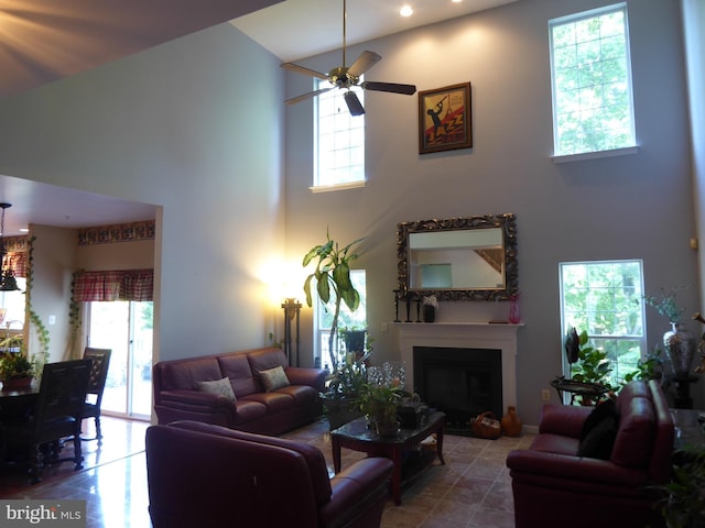 living area with a high ceiling, ceiling fan, a fireplace, and tile patterned floors
