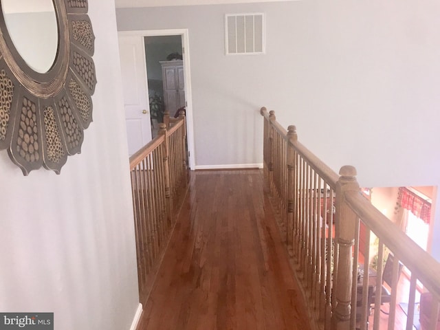 hallway featuring wood finished floors, baseboards, and an upstairs landing