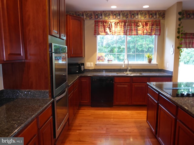 kitchen with a sink, black appliances, dark stone counters, light wood-type flooring, and recessed lighting