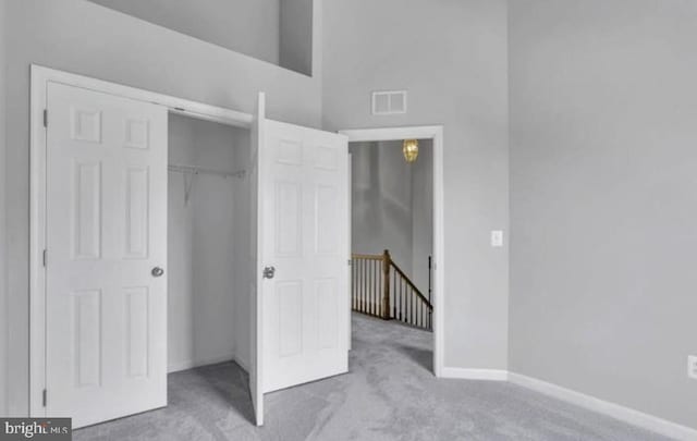 unfurnished bedroom featuring carpet, a closet, baseboards, and a high ceiling