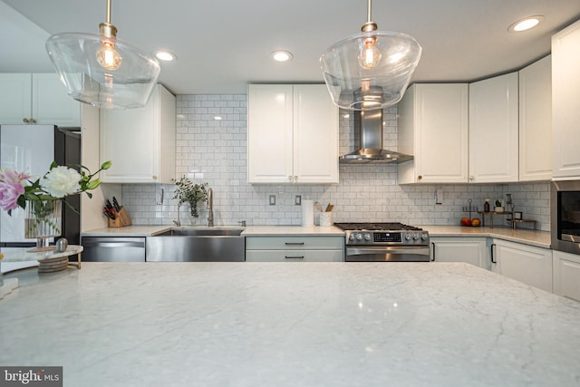 kitchen featuring wall chimney range hood, stainless steel appliances, a sink, white cabinets, and decorative backsplash