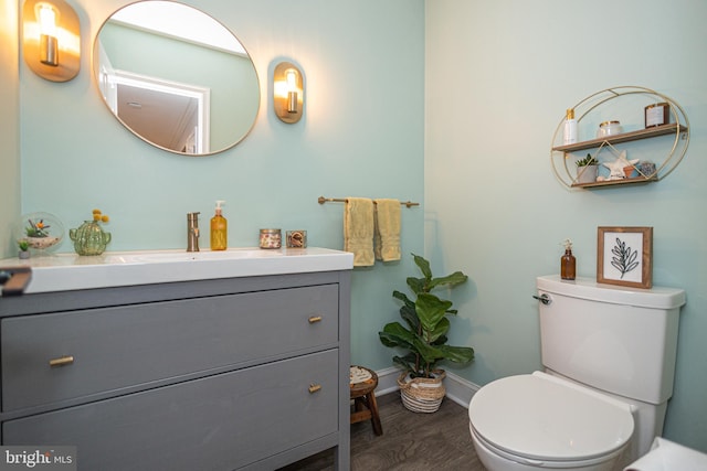 half bath featuring toilet, baseboards, vanity, and wood finished floors