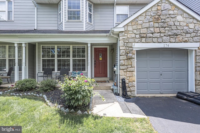 property entrance with stone siding, an attached garage, covered porch, and driveway