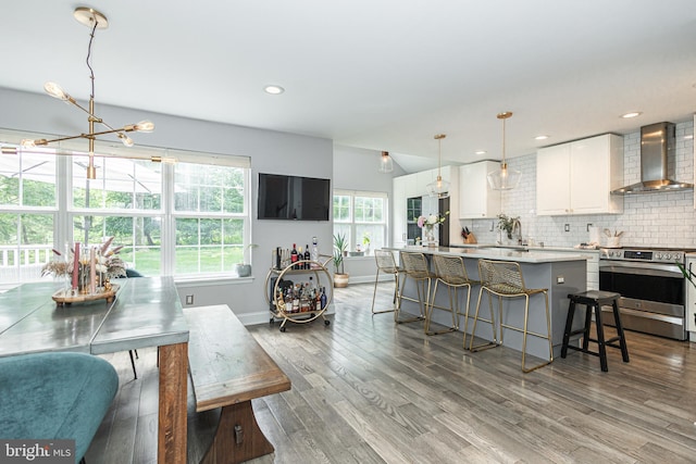 kitchen featuring wall chimney range hood, electric range, backsplash, white cabinets, and wood finished floors