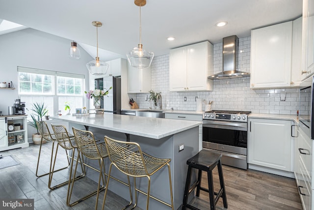 kitchen with wall chimney range hood, stainless steel appliances, a sink, tasteful backsplash, and dark wood-style floors