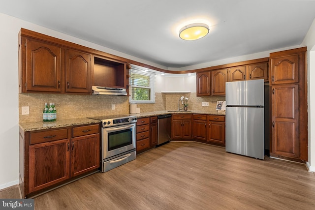 12516 Castleleigh Pl, Silver Spring, MD 20904 - kitchen featuring appliances with stainless steel finishes, under cabinet range hood, light wood-type flooring, light stone countertops, and tasteful backsplash