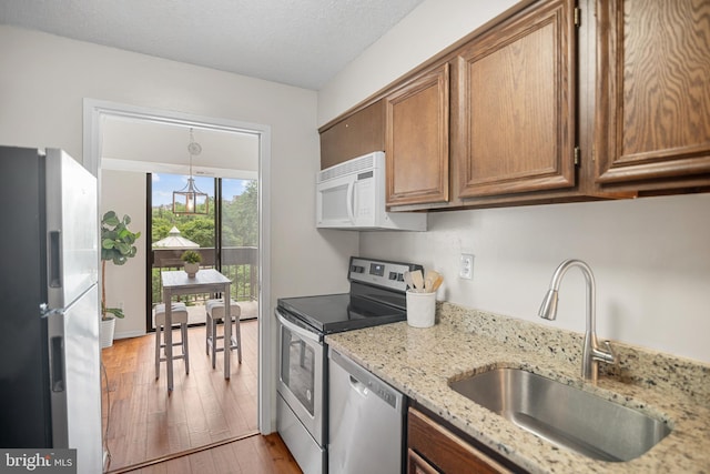 5300 Holmes Run Pkwy Unit 403, Alexandria, VA 22304 - kitchen featuring appliances with stainless steel finishes, a sink, light wood-type flooring, brown cabinets, and light stone countertops