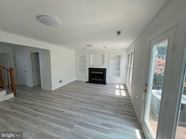 6325 Powder Flask Ct, Centreville, VA 20121 - unfurnished living room with built in shelves, light wood-type flooring, stairs, baseboards, and a fireplace with flush hearth
