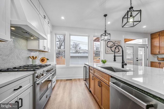 kitchen with appliances with stainless steel finishes, custom exhaust hood, a sink, light wood finished floors, and brown cabinetry