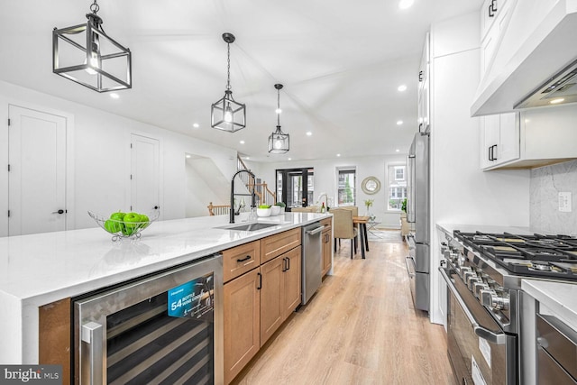 kitchen with wine cooler, under cabinet range hood, a sink, high end appliances, and light wood finished floors
