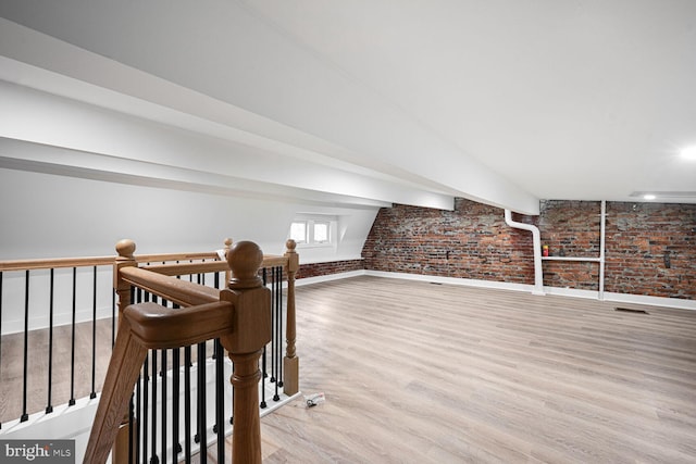 additional living space with wood finished floors, brick wall, and baseboards
