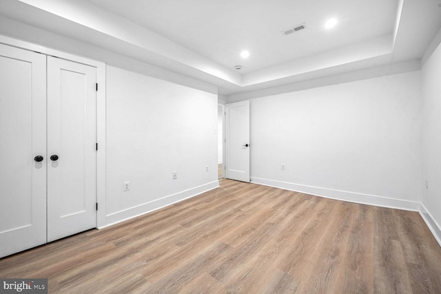 unfurnished bedroom with a tray ceiling, light wood-style floors, baseboards, a closet, and recessed lighting