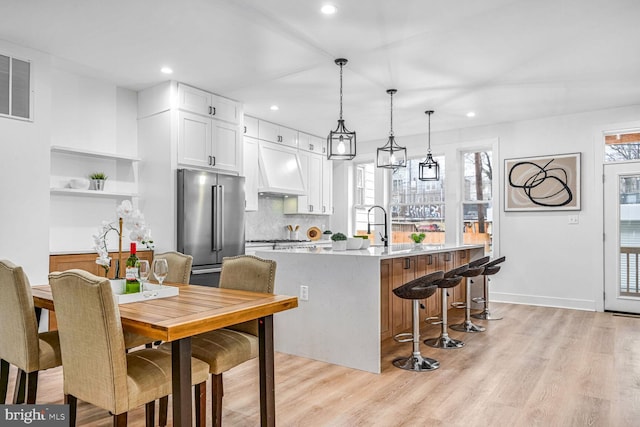 kitchen featuring high end refrigerator, premium range hood, white cabinets, light wood-type flooring, and recessed lighting