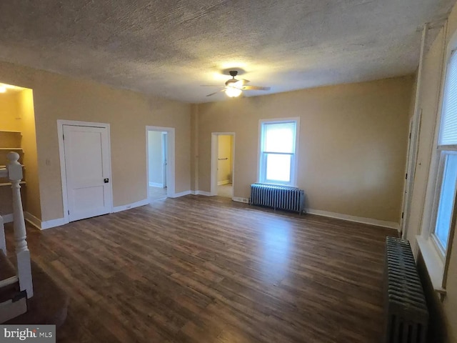 unfurnished living room with radiator heating unit, ceiling fan, dark wood-style floors, a textured ceiling, and baseboards