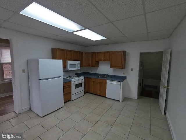 kitchen with white appliances, a drop ceiling, a sink, dark countertops, and baseboards