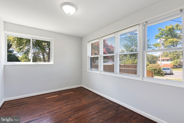 empty room with baseboards, healthy amount of natural light, and dark wood-type flooring