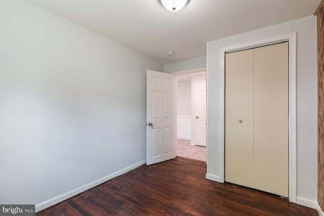 unfurnished bedroom featuring dark wood-style flooring, baseboards, and a closet