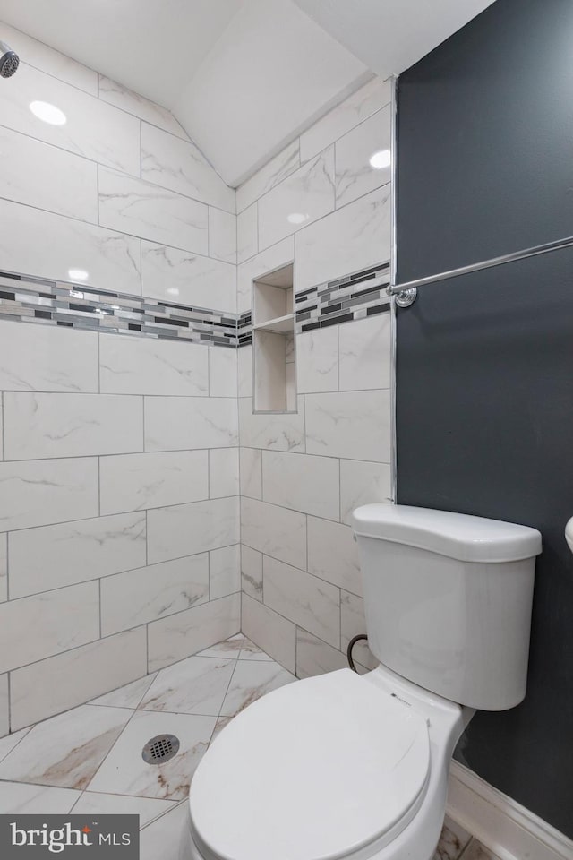 bathroom with marble look tiles, vaulted ceiling, toilet, and tiled shower