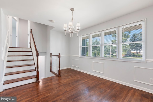unfurnished room featuring wood finished floors, a chandelier, baseboards, and stairway
