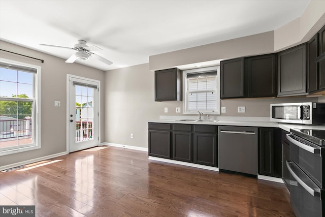 kitchen featuring stainless steel appliances, a sink, ceiling fan, light countertops, and dark wood-type flooring
