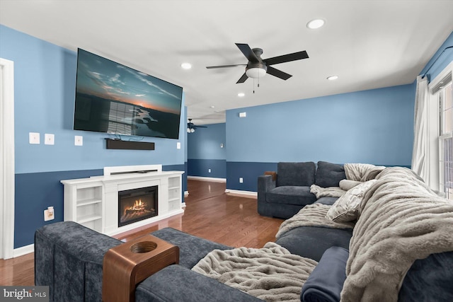 living room featuring ceiling fan, recessed lighting, baseboards, wood finished floors, and a lit fireplace
