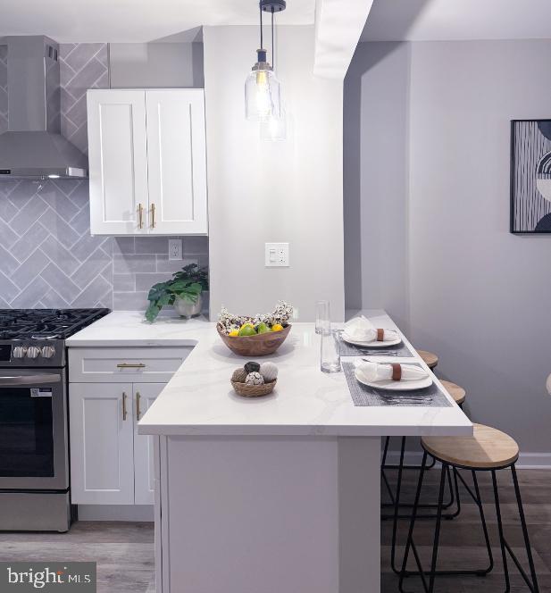 185 La Cascata, Clementon, NJ 08021 - kitchen with wall chimney range hood, stainless steel gas range oven, a peninsula, a kitchen breakfast bar, and white cabinetry