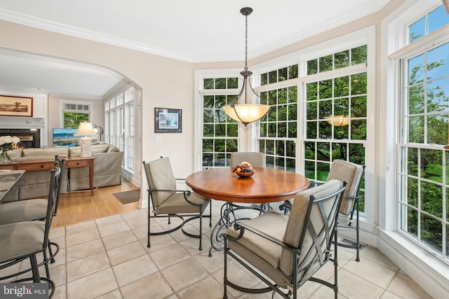 dining space with arched walkways, ornamental molding, light tile patterned floors, and a lit fireplace