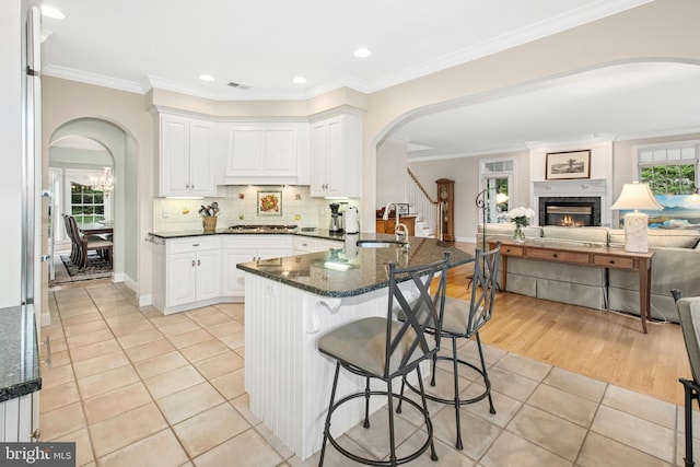 kitchen with a sink, open floor plan, arched walkways, stainless steel gas stovetop, and a breakfast bar
