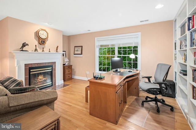 office area with light wood-style floors, a tile fireplace, and baseboards