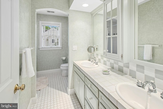 bathroom with toilet, double vanity, tasteful backsplash, and baseboards