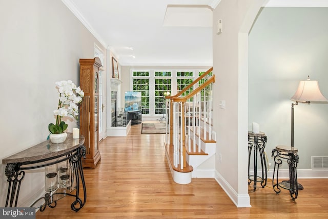 hallway featuring light wood-style floors, stairs, ornamental molding, arched walkways, and baseboards