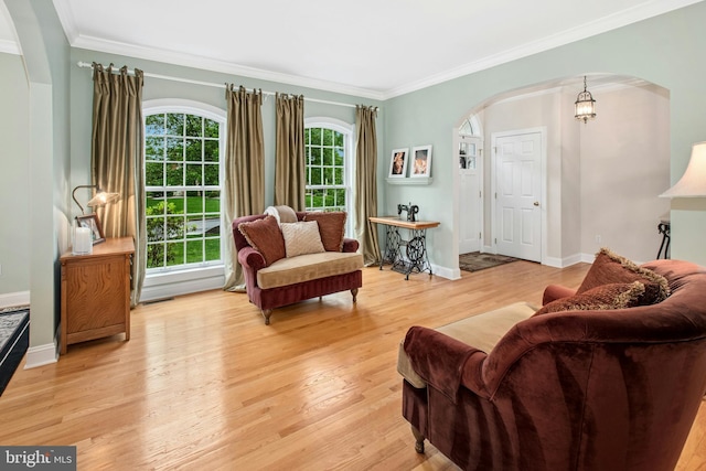 living area featuring arched walkways, crown molding, light wood-style floors, and baseboards