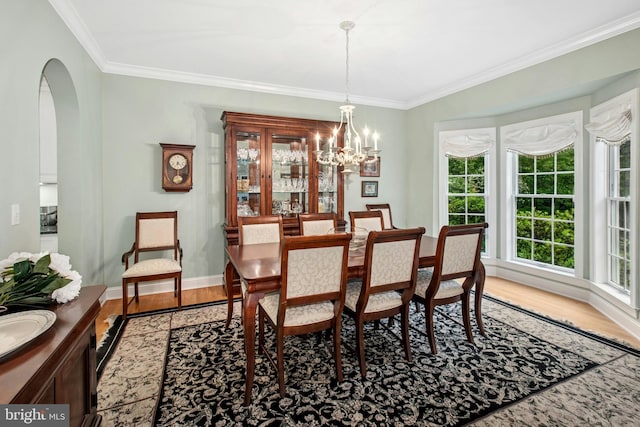 dining area with light wood-style floors, a chandelier, crown molding, arched walkways, and baseboards