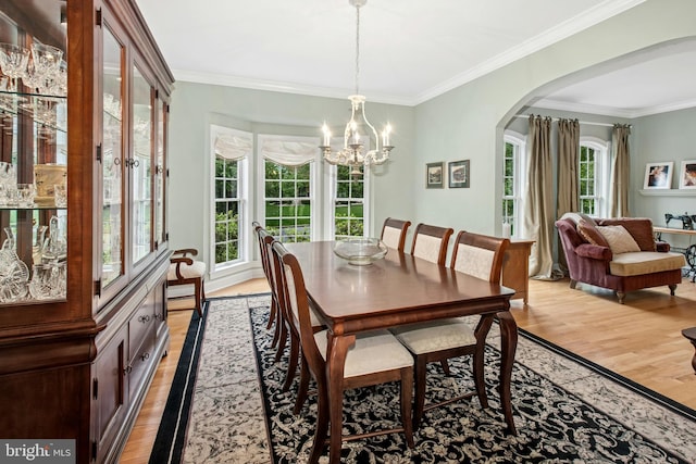 dining area with light wood-style flooring, a chandelier, arched walkways, and crown molding